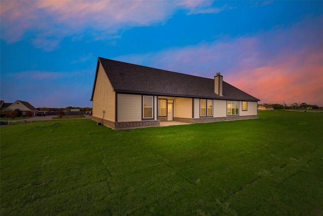 back house at dusk featuring a yard and a patio area