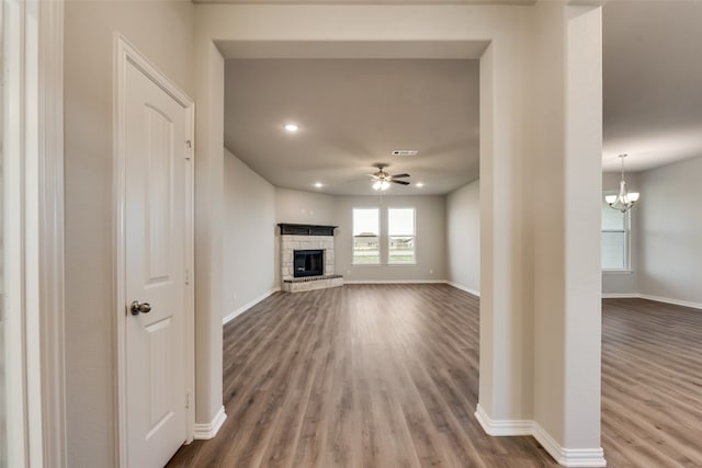 unfurnished living room with a stone fireplace, ceiling fan with notable chandelier, and dark hardwood / wood-style flooring