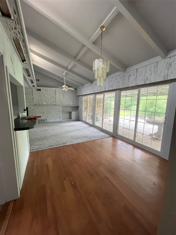 unfurnished living room featuring ceiling fan with notable chandelier, hardwood / wood-style flooring, and lofted ceiling with beams