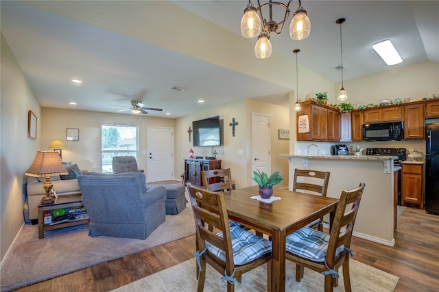 dining area featuring dark hardwood / wood-style flooring, ceiling fan with notable chandelier, vaulted ceiling, and sink