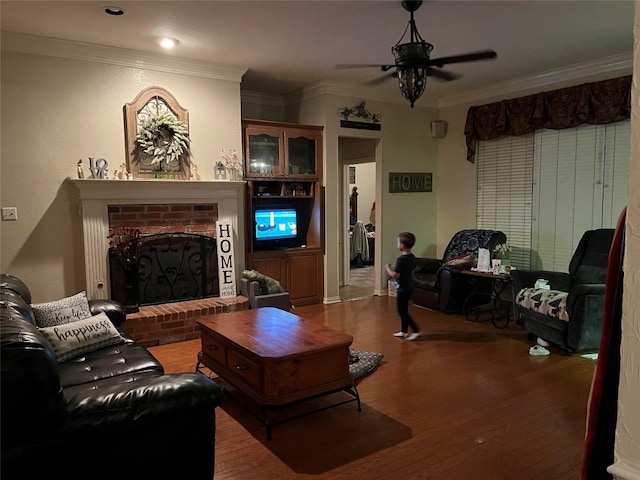 living room featuring a fireplace, hardwood / wood-style floors, ceiling fan, and crown molding