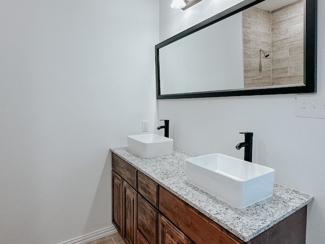 bathroom with dual vanity and tiled shower