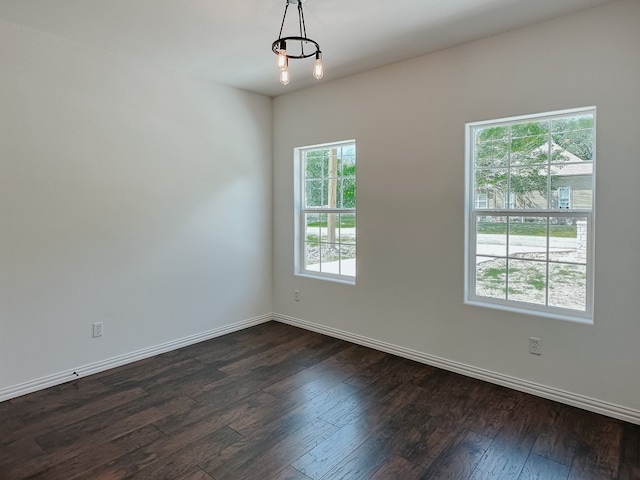 spare room featuring a chandelier, dark hardwood / wood-style floors, and a wealth of natural light