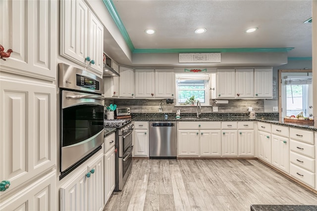 kitchen featuring appliances with stainless steel finishes, backsplash, sink, light hardwood / wood-style flooring, and white cabinets