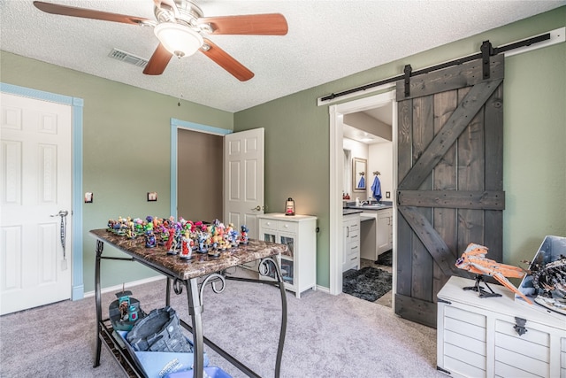 office with a barn door, light carpet, a textured ceiling, and ceiling fan