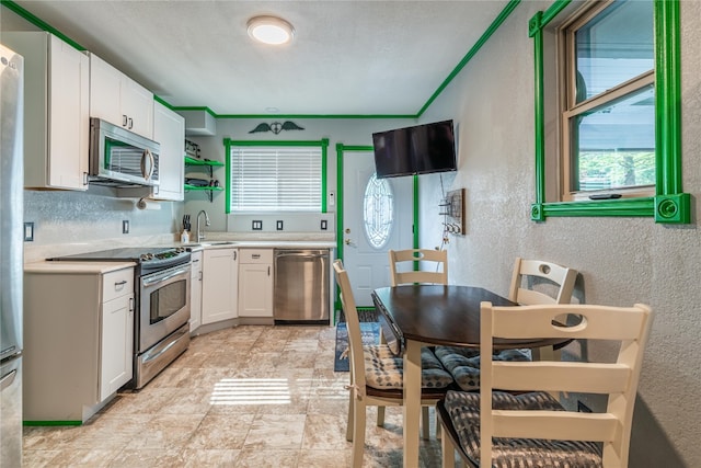 kitchen with sink, stainless steel appliances, light tile floors, white cabinets, and crown molding