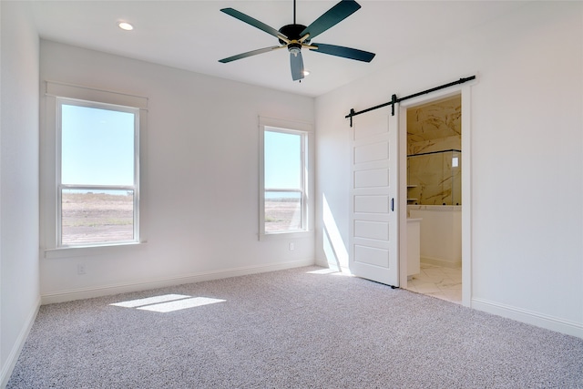 unfurnished bedroom with ensuite bathroom, ceiling fan, a barn door, and light colored carpet