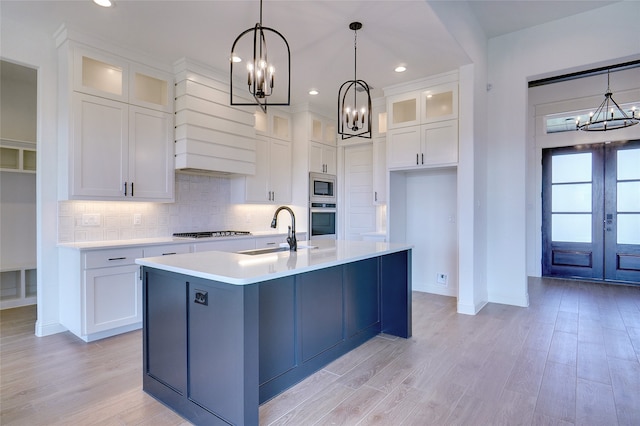 kitchen with appliances with stainless steel finishes, light hardwood / wood-style flooring, sink, decorative backsplash, and an island with sink