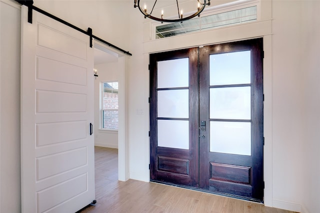 foyer featuring an inviting chandelier, light wood-type flooring, french doors, and a barn door