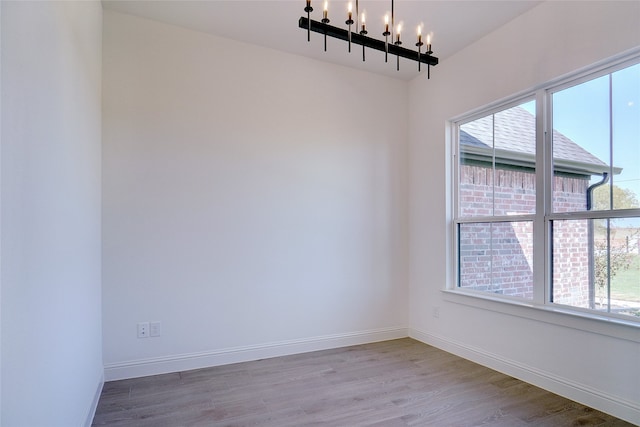 empty room with wood-type flooring, a notable chandelier, and plenty of natural light