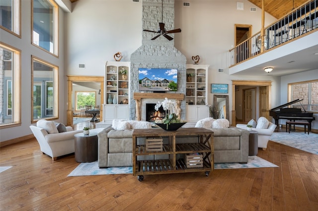 living room with ceiling fan, a large fireplace, a high ceiling, and light wood-type flooring