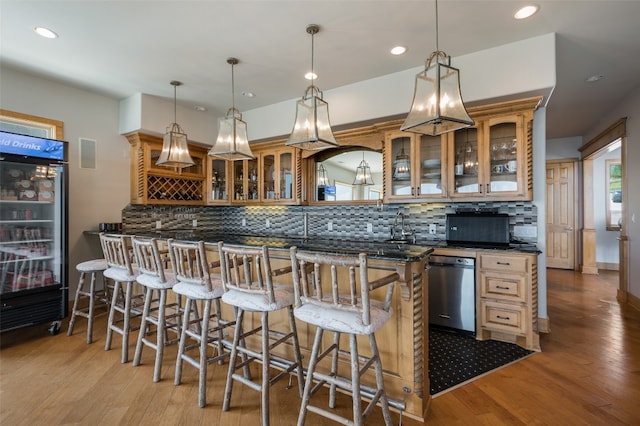 kitchen featuring backsplash, a kitchen bar, dishwashing machine, and decorative light fixtures