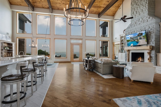 living room with beam ceiling, a fireplace, ceiling fan with notable chandelier, high vaulted ceiling, and wooden ceiling