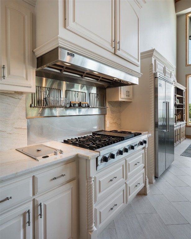 kitchen featuring appliances with stainless steel finishes, light stone counters, white cabinets, light tile floors, and backsplash