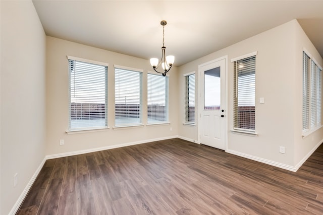 unfurnished dining area featuring a notable chandelier, plenty of natural light, and dark hardwood / wood-style floors