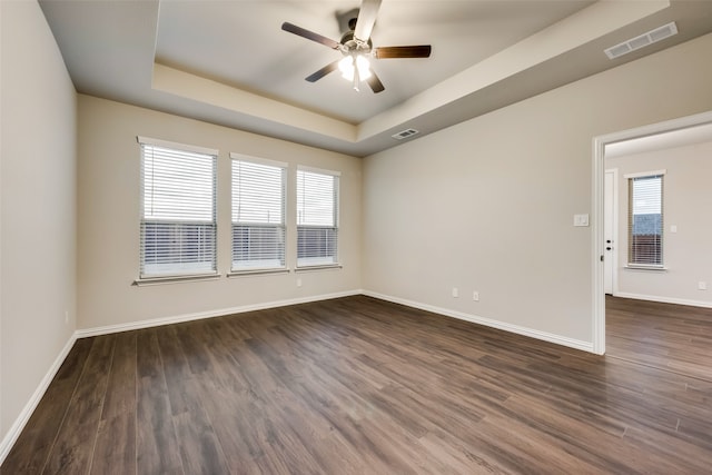 empty room featuring a raised ceiling, a wealth of natural light, ceiling fan, and dark wood-type flooring