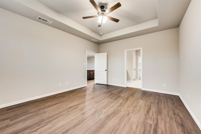 empty room featuring hardwood / wood-style flooring, a raised ceiling, and ceiling fan