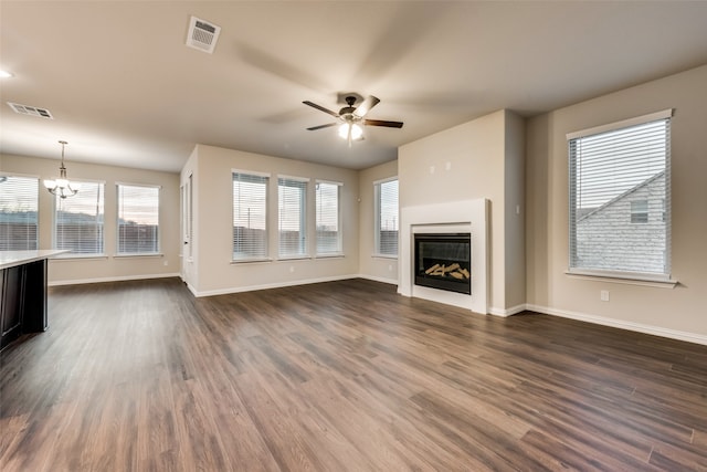 unfurnished living room with ceiling fan with notable chandelier, a healthy amount of sunlight, and dark hardwood / wood-style floors