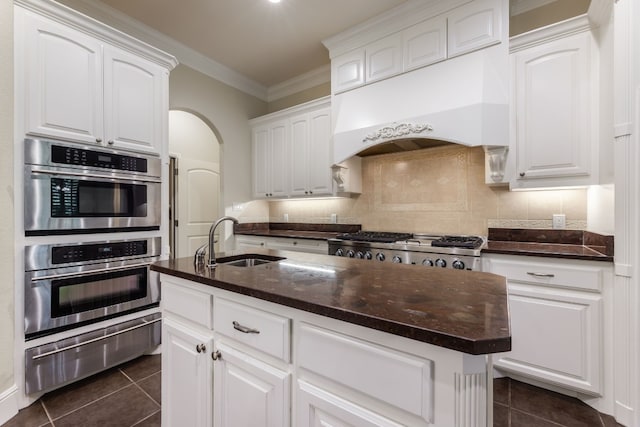 kitchen featuring custom exhaust hood, tasteful backsplash, white cabinets, a kitchen island with sink, and sink