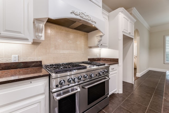 kitchen featuring dark tile floors, backsplash, custom exhaust hood, white cabinetry, and range with two ovens