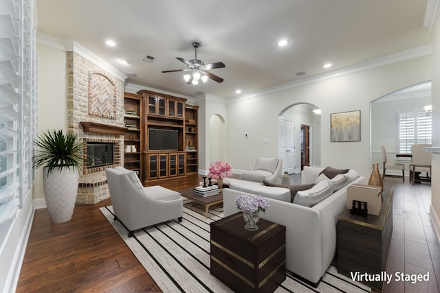 living room featuring ceiling fan, a fireplace, brick wall, crown molding, and dark hardwood / wood-style flooring