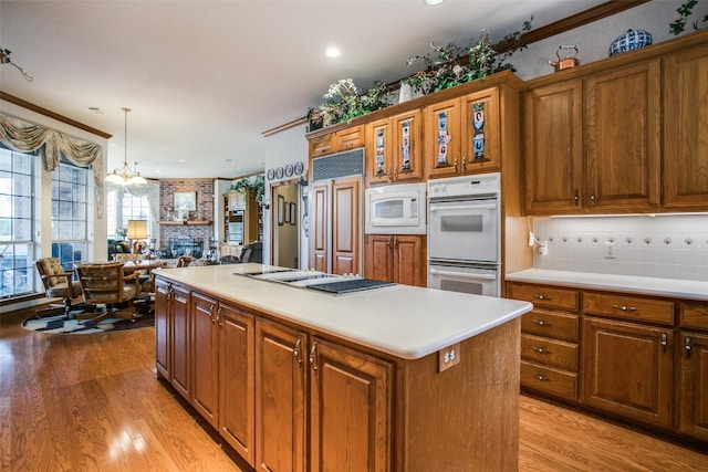 kitchen with hanging light fixtures, backsplash, light hardwood / wood-style flooring, a chandelier, and built in appliances