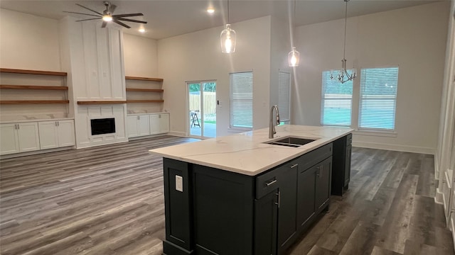 kitchen featuring a high ceiling, ceiling fan with notable chandelier, dark hardwood / wood-style floors, a kitchen island with sink, and sink