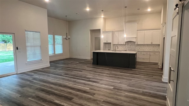 kitchen with a kitchen island with sink, dark hardwood / wood-style flooring, white cabinetry, backsplash, and sink