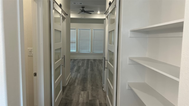 spacious closet featuring dark hardwood / wood-style floors, ceiling fan, and a barn door