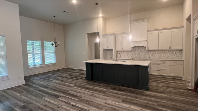 kitchen with backsplash, an island with sink, white cabinetry, sink, and dark hardwood / wood-style flooring