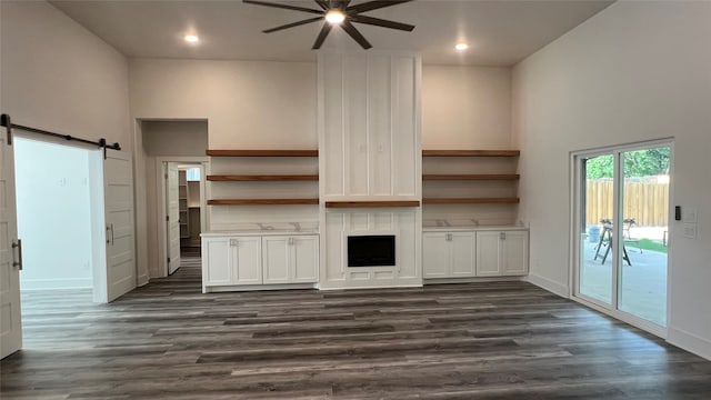 unfurnished living room with a barn door, dark wood-type flooring, ceiling fan, and a high ceiling