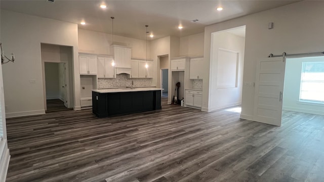 kitchen with tasteful backsplash, a barn door, dark hardwood / wood-style floors, and an island with sink