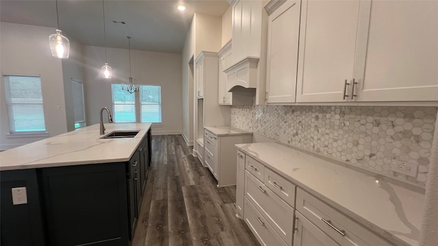 kitchen with light stone counters, dark wood-type flooring, backsplash, a center island with sink, and sink