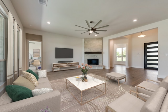 living room featuring hardwood / wood-style floors, ceiling fan, and a stone fireplace