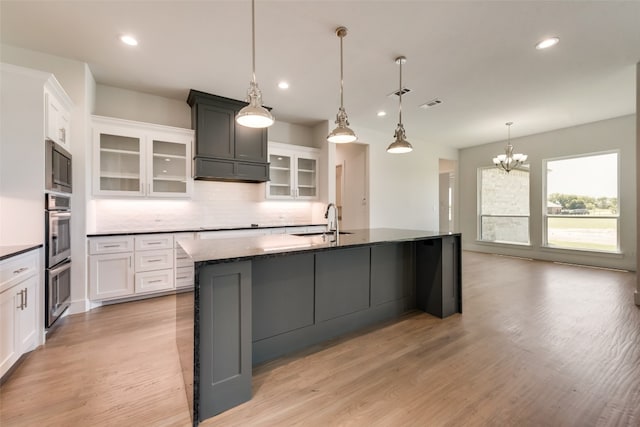 kitchen with a large island with sink, an inviting chandelier, white cabinets, sink, and decorative light fixtures