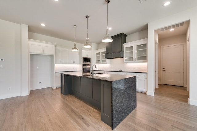 kitchen with backsplash, built in microwave, white cabinets, oven, and an island with sink