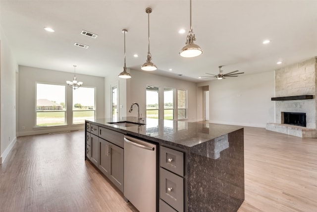 kitchen with stainless steel dishwasher, dark stone counters, a kitchen island with sink, sink, and decorative light fixtures