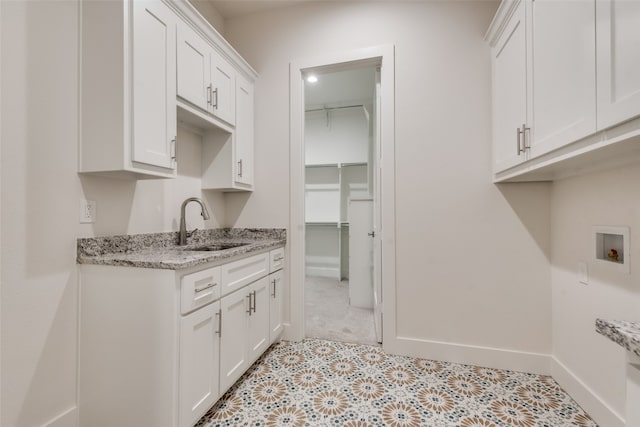 kitchen with light stone counters, white cabinetry, and sink