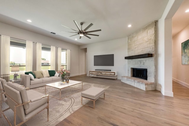 living room featuring ceiling fan, light hardwood / wood-style floors, and a stone fireplace