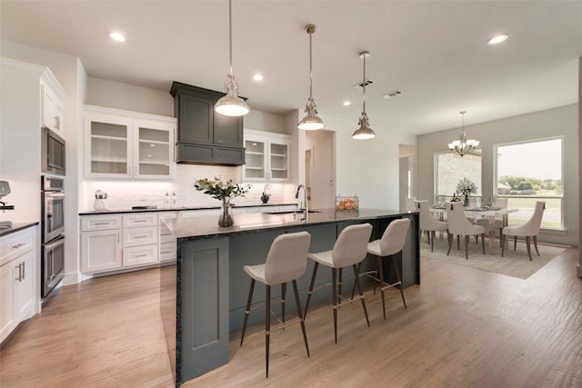 kitchen featuring white cabinetry, sink, hanging light fixtures, an inviting chandelier, and a large island with sink