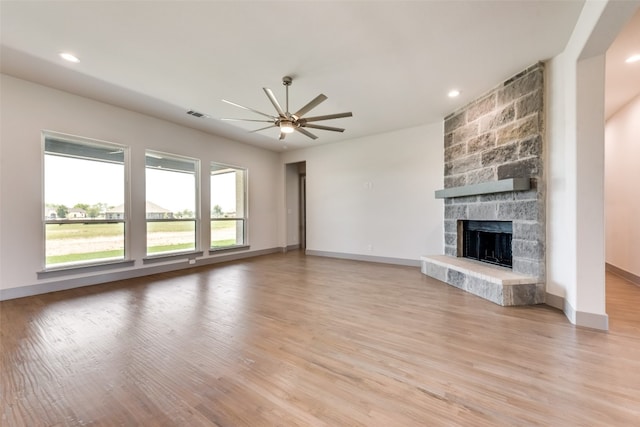 unfurnished living room featuring light hardwood / wood-style flooring, a stone fireplace, and ceiling fan