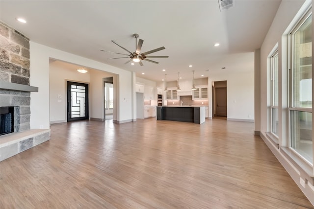 unfurnished living room with ceiling fan, a fireplace, and light hardwood / wood-style floors