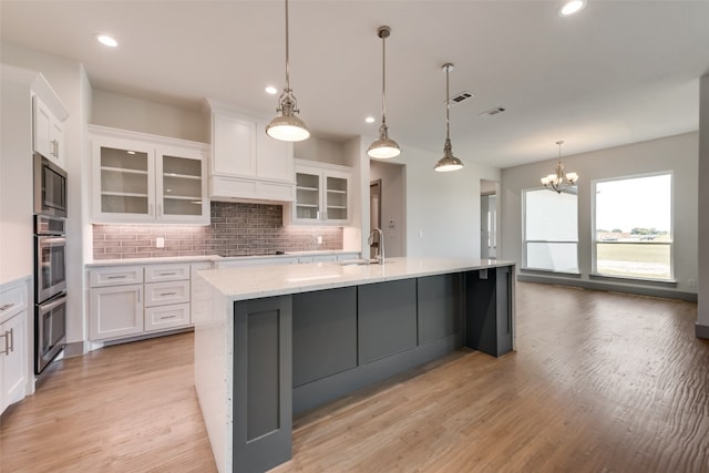 kitchen with a notable chandelier, backsplash, white cabinets, sink, and a large island