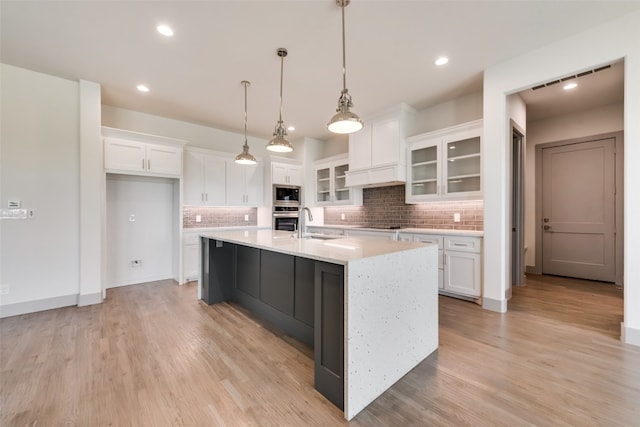 kitchen with decorative light fixtures, stainless steel oven, white cabinetry, and an island with sink