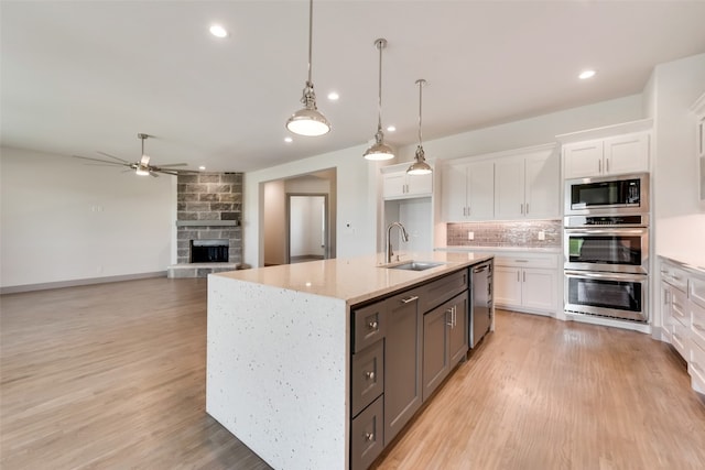 kitchen featuring stainless steel appliances, backsplash, decorative light fixtures, a center island with sink, and white cabinets