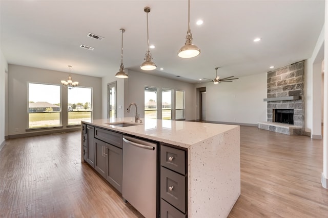 kitchen featuring dishwasher, a kitchen island with sink, ceiling fan with notable chandelier, a stone fireplace, and sink