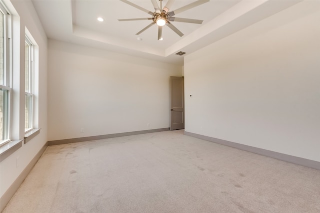 spare room with ceiling fan, light carpet, and a tray ceiling