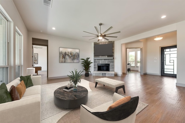 living room featuring hardwood / wood-style flooring, a stone fireplace, and ceiling fan