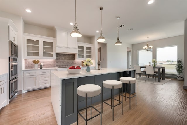 kitchen featuring white cabinets, decorative backsplash, pendant lighting, and a kitchen island with sink