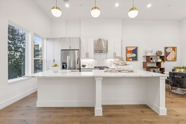 kitchen with pendant lighting, stainless steel appliances, a wealth of natural light, and wall chimney exhaust hood